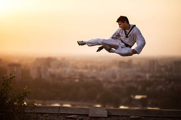Teakwondo fighter performing high kick while being in mid air at sunset in fly-kick pose.