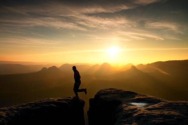 istock Hiker in black is jumping between mountains peaks. 546461154