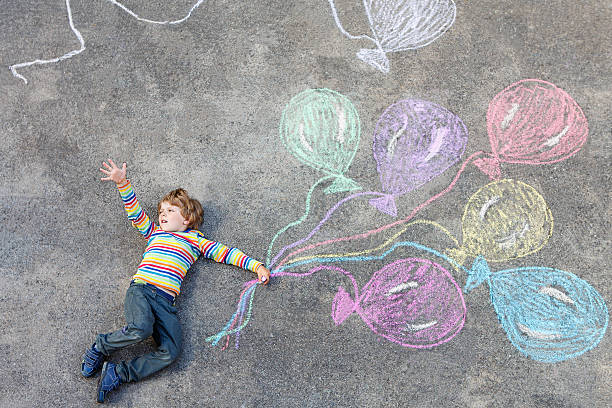 istock Kid boy having fun with colorful balloons drawing with chalks 546463768