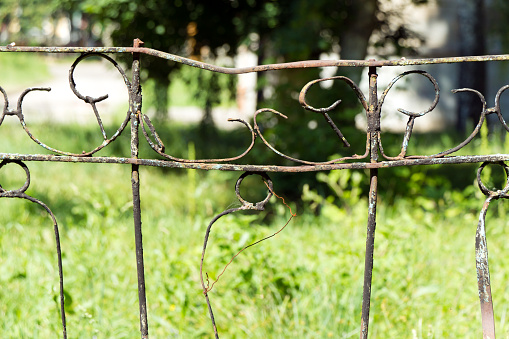 A fence made of rusty metal rods. Very old and rusty. A long time outdoors. The background is blurred (green grass).