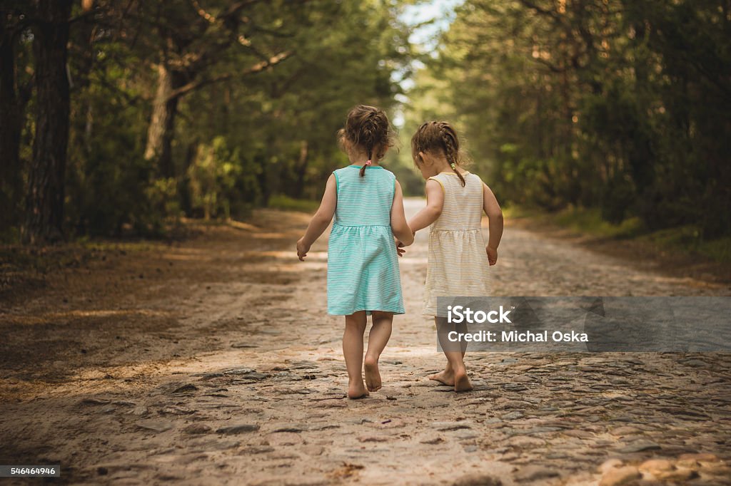 Two little girls on a forest road Photo of two cute twins walking along a forest road Child Stock Photo