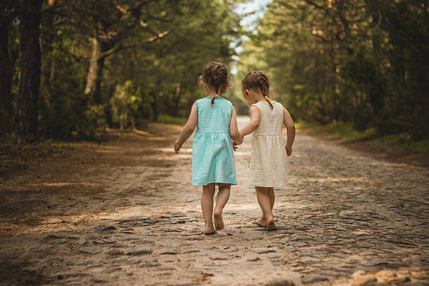 Two little girls on a forest road Photo of two cute twins walking along a forest road sister stock pictures, royalty-free photos & images