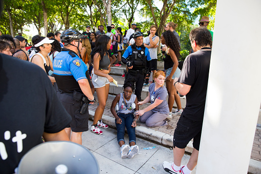Fort Lauderdale, United States - July 9, 2016: A young adult female protestor collapses from heat exhaustion during the black lives matter rally. She is being assisted by police and fire rescue.