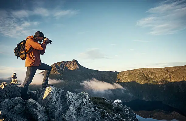Shot of a young man taking photographs while hiking in the mountains