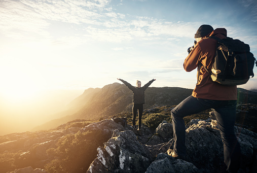 Shot of a young man taking photos of his girlfriend while hiking in the mountains