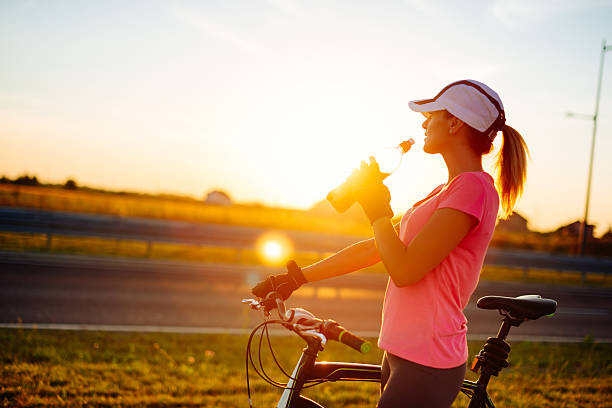 Portrait of beautiful muscular woman holding grips of bike steering bar on sunny summer day in sunset, after exhausting ride and drinking energy drink. Woman is wearing cap and dressed in sports clothing. Location: Novi Sad, Serbia, Europe