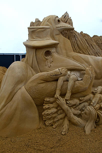 istock Sand sculpture of figures wearing a plague mask. 546784248