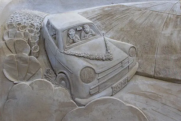 Sand sculpture of a car with a family driving between fields of flowers. With the car driving around the corner towards the front.This sand sculpture is made by Bouke Atema and photograped by Bouke Atema.