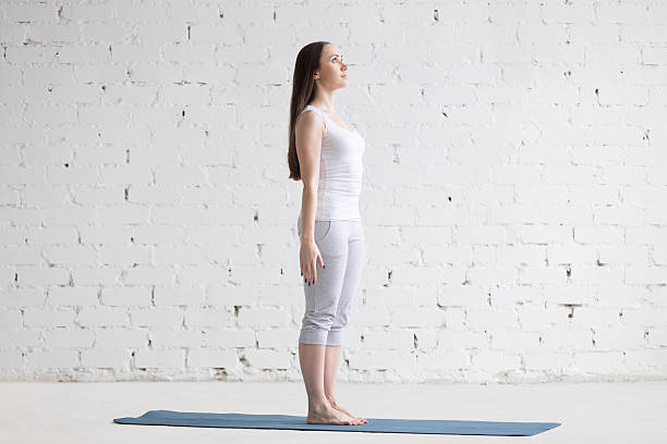 Beautiful sporty young woman doing Tadasana pose in white loft Attractive happy young woman working out indoors. Side view portrait of beautiful model doing yoga exercise on blue mat. Standing in Tadasana, Mountain Pose. Full length good posture stock pictures, royalty-free photos & images