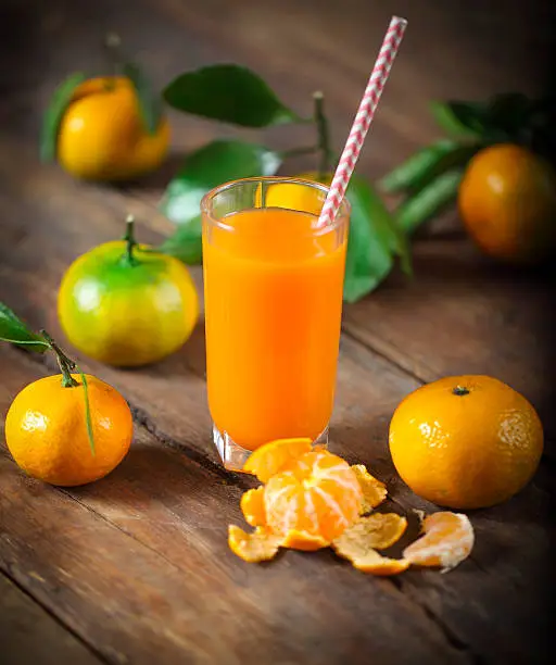 Glass of fresh tangerine juice with ripe tangerines, leaves and old-fashioned straw