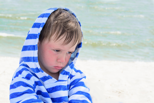 Little cute kid hurt and pouted, disappointed. Beautiful little kid with atopic dermatitis on the background of the sea