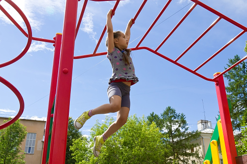 Little girl playing on a playground, hanging walk along the monkey bars on the sky background