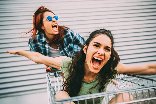 Two young girls having fun with a shopping cart.