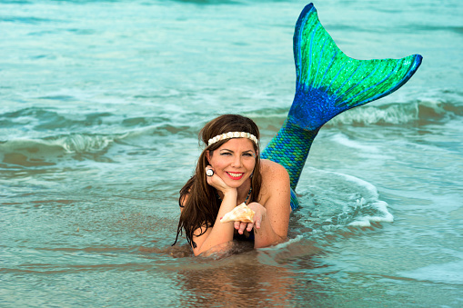 Woman in late 30's dressed up as a mermaid with a blue and green tail swims in the Atlantic Ocean, Vilano Beach, St. Augustine, Florida, USA