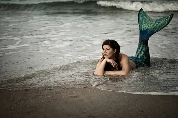 Woman in late 30's dressed up as a mermaid lies in shallow water at the Atlantic Ocean, Vilano Beach, St. Augustine, Florida, USA