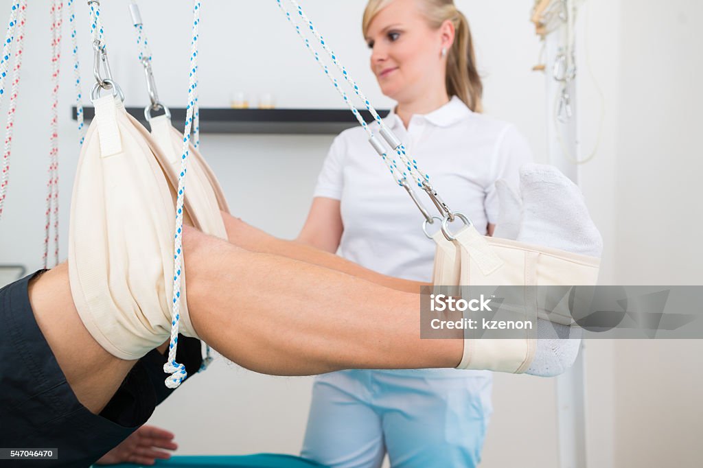 Physiotherapist with patient on sling table Patient at the physiotherapy doing physical exercises with his therapist on sling table Adult Stock Photo