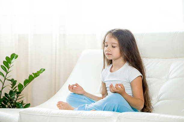Happy kid girl doing yoga at home Healthy lifestyle concept. Yoga and Fitness. Serene yoga little girl working out in living room on white coach. Beautiful funny kid girl sitting cross-legged on home sofa, meditating with closed eyes sukhasana stock pictures, royalty-free photos & images