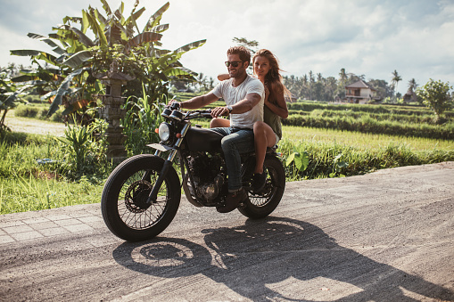 Outdoor shot of young couple riding motorbike. Man riding on a motorcycle with girlfriend on rural road.