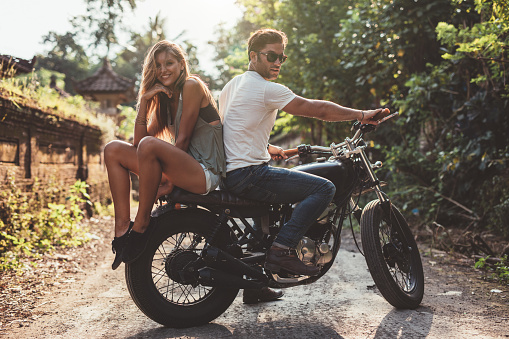 Beautiful young couple on a motorbike. Young man and woman on motorcycle in a village.