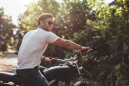 Portrait of handsome young man on motorcycle. Happy caucasian male on motorbike looking away and smiling.