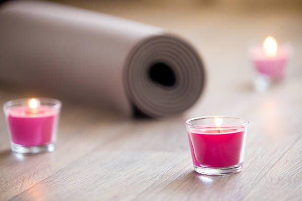 Lighted pink candle and rolled brown yoga, pilates mat
