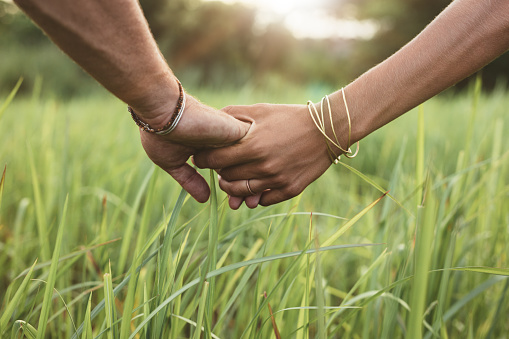 Close up shot of man and woman holding hands in grass field. Young couple in love with hand in hand.