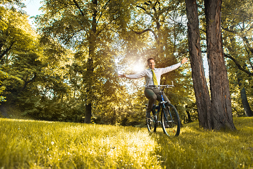 Happy mid adult businessman having fun while riding a bike with his arms outstretched.