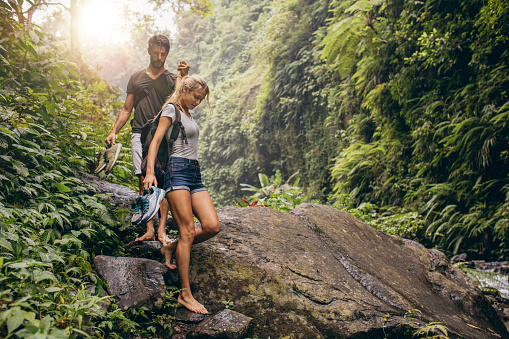 Shot of young couple walking through the mountain trail. Man and woman hiking on mountain trail barefoot.