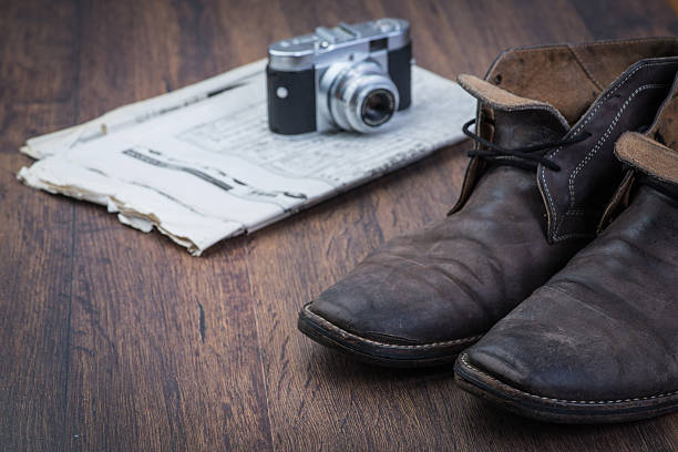 Old worn out brown leather shoes with camera and newspaper over the brown background