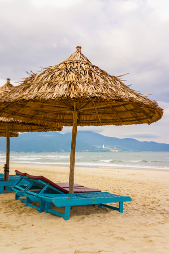 Palm shelter and sunbeds at the China Beach in Danang, Vietnam. It is also called Non Nuoc Beach. South China Sea on the background.
