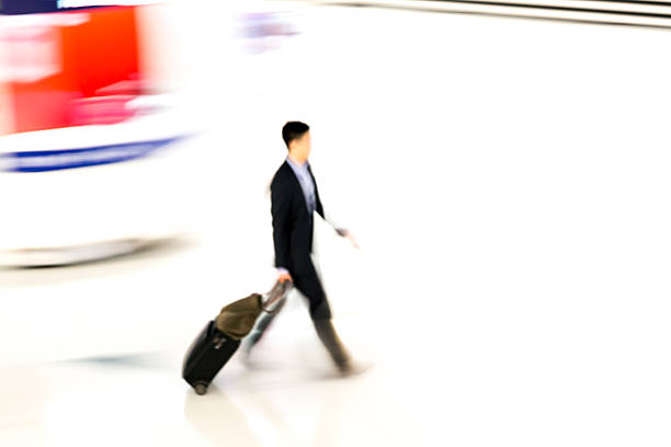 motion blurred, unrecognizable businessmen rushing through airport, pulling luggage, elevated view