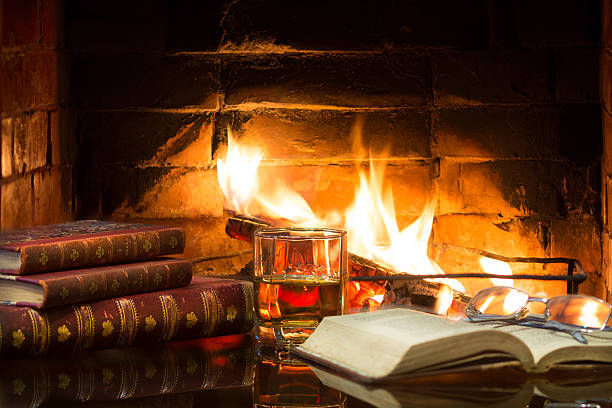 istock Glass alcoholic drink wine antique books in front warm fireplace. 547142810