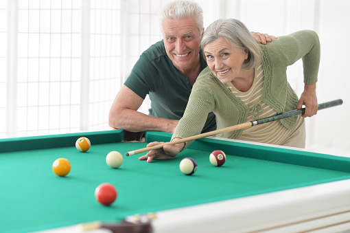 Amusing old couple on vacation playing billiard