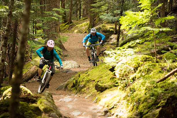 Couple mountain biking through a forest Couple mountain biking through a forest mountain biking stock pictures, royalty-free photos & images