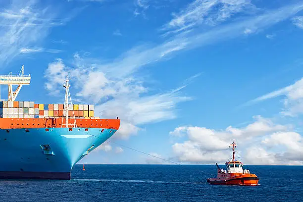 Tugboat towing a large container ship on sea.