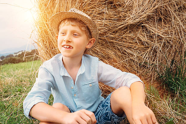 istock Boy sits near big haystack on the field 547164134