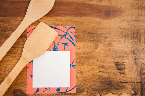 Wooden kitchen tools, spoon, spatula on wooden kitchen table with blank adhesive notepad for your copy.  Notepad on unique red and blue background.