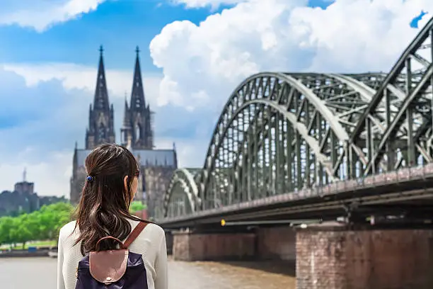 Young woman seen from back looking to rhine river, huge bridge and famous cathedral of Cologne, Germany
