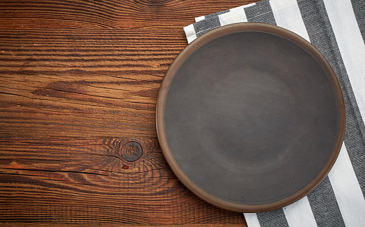 napkin and dark plate on brown wooden table, top view