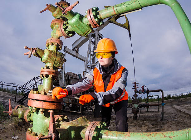 Woman engineer in the oil field repairing wellhead Woman engineer in the oil field repairing wellhead with the wrench wearing orange helmet and work clothes. Oil and gas concept. wellhead stock pictures, royalty-free photos & images