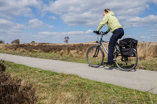 Biker on a cycle path Elspeet, The Netherlands - April 8, 2012: Woman on a bike in the nature reserve Elspeetsche Heide. molinia caerulea stock pictures, royalty-free photos & images