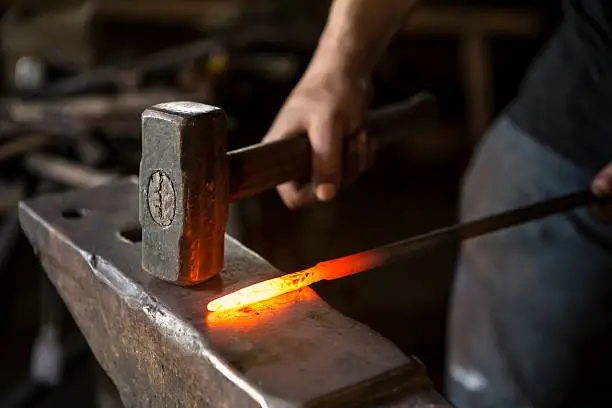 close-up picture of blacksmith working. glowing metal and hammer.