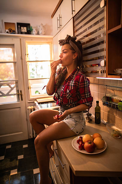 красивая очаровательная девушка ест клубнику на кухне. - pin up girl 1960s style desire elegance стоковые фото и изображения