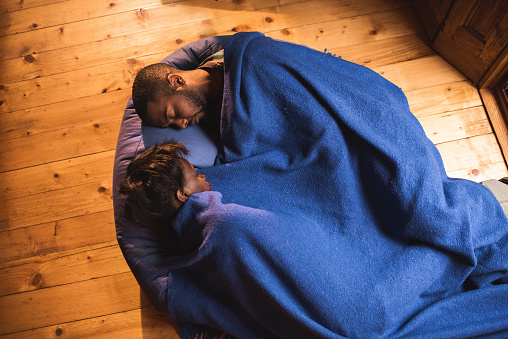 High angle view of African American couple taking a nap on a bean bag while being covered with blanket. Focus is on man.