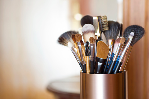 Makeup brushes in metal stand over blurred abstract room background