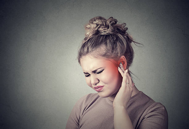 Tinnitus. Sick female having ear pain Tinnitus. Closeup up side profile sick female having ear pain touching her painful head colored in red isolated on gray background neuralgia stock pictures, royalty-free photos & images