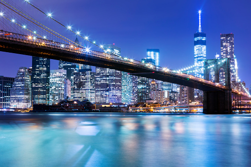 New York skyline with Brooklyn Bridge illuminated at night. In the background is seen Manhattan skyline with the One World Trade Center - Freedom Tower and Beekman Tower on the right side, the tallest residential tower in world, designed by Frank Gehry. horizontal orientation, America, USA.