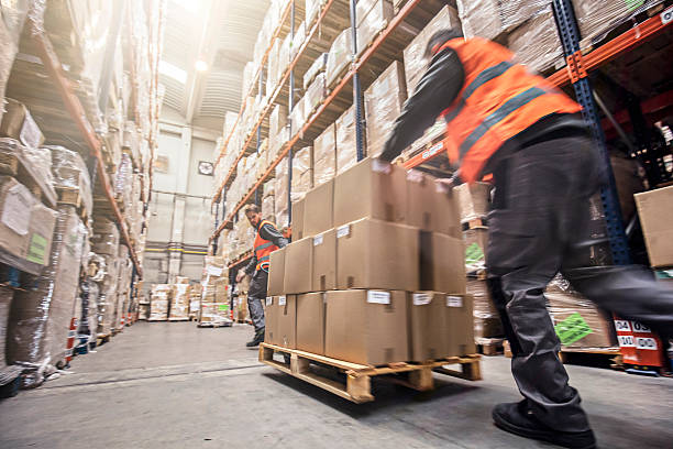 motion blur of two men moving boxes in a warehouse - armazém de distribuição imagens e fotografias de stock