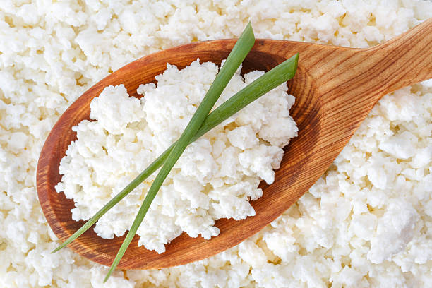 crumbly cottage cheese in the wooden spoon with onion stock photo