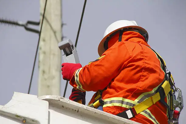 A linesman checks data on a wireless voltage reader used to gauge current through electric lines. 